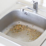 A dirty clogging kitchen sink drain with food particles.