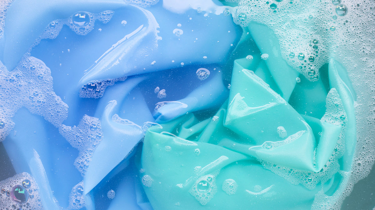 Blue and green fabric submerged in soapy water.