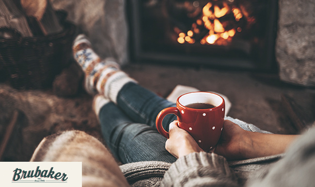 A person holding a hot drink and reclining by a fire. 