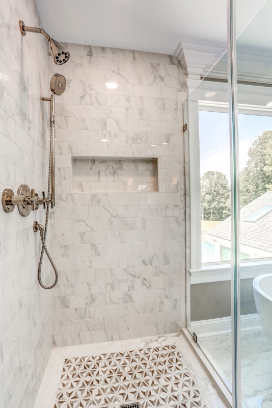 beautiful marble shower with intricate flooring tile and recessed wall nook for soap and shampoo